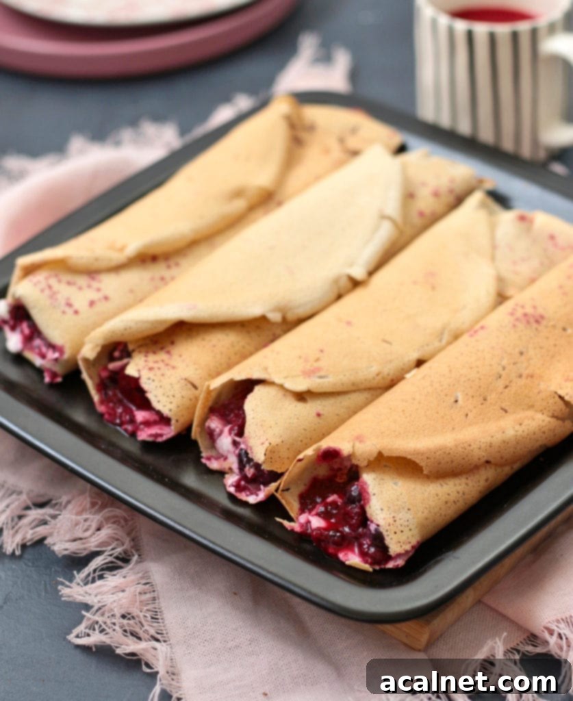Delicate Buckwheat Crêpes generously filled with a vibrant berry compote, artfully presented on a black plate.