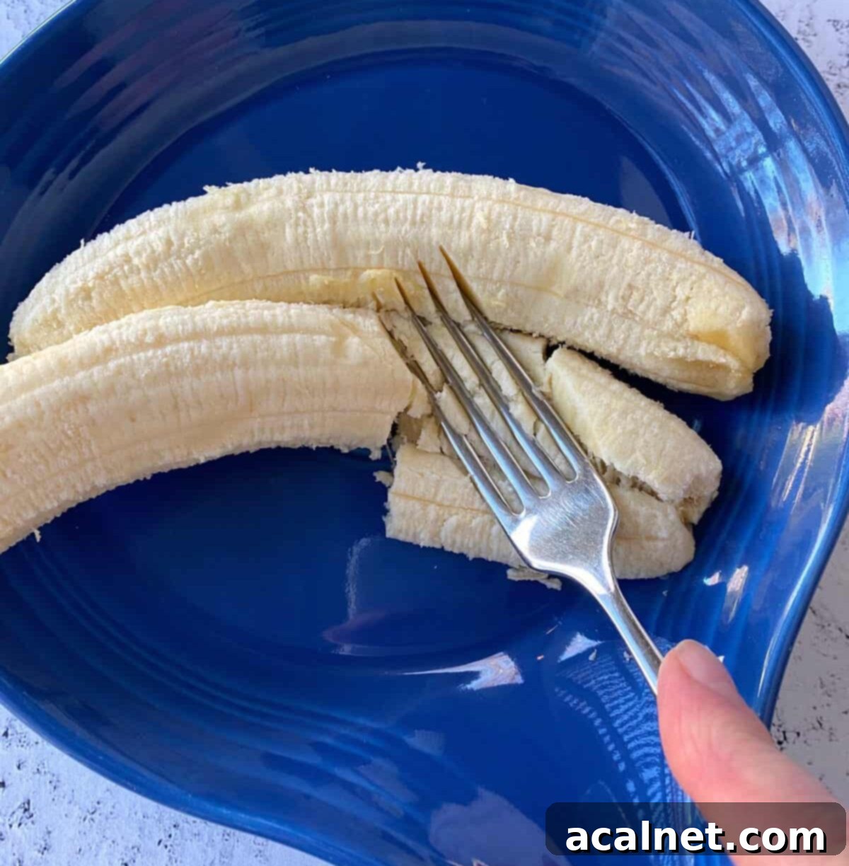 Two bananas in a dish, with a fork mashing them.