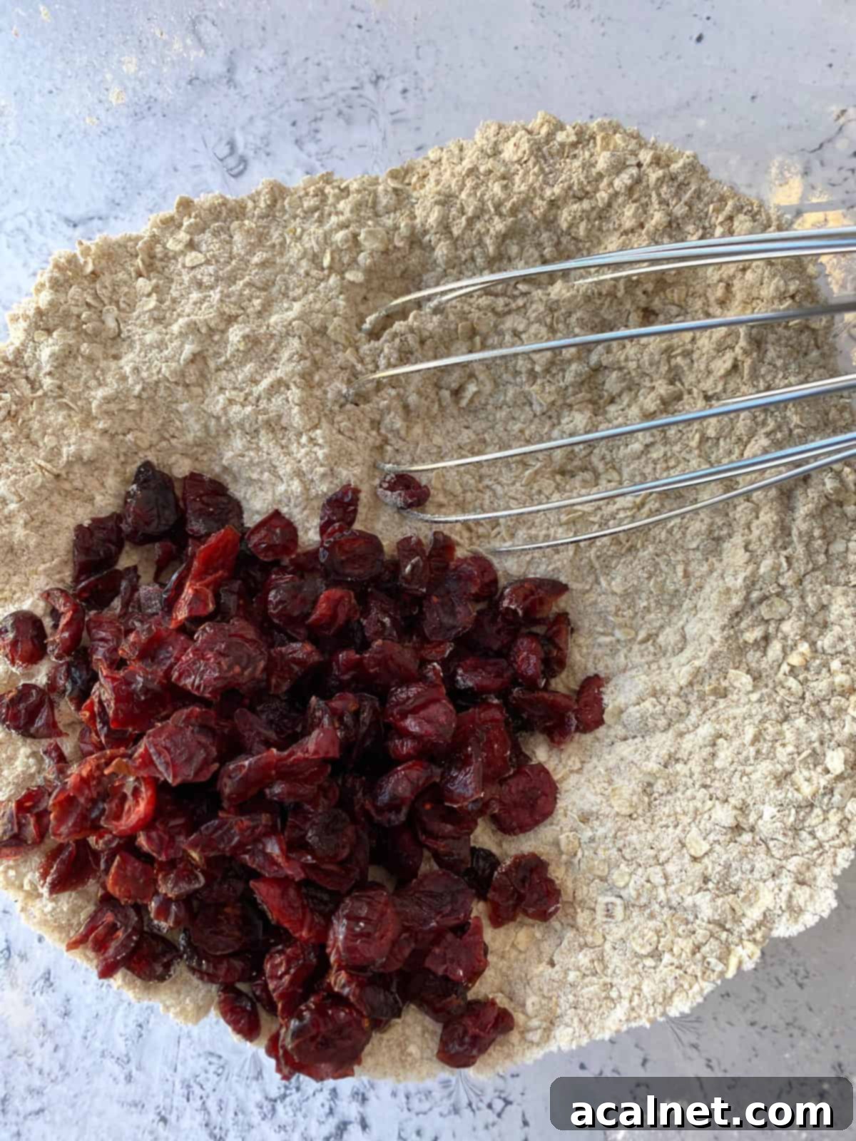 Dried cranberries and dry ingredients in a bowl with a whisk.