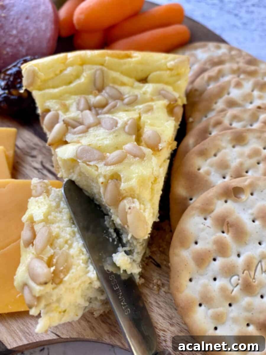 A wedge of savory cheesecake with crackers, cheddar cheese, carrots and a small knife on a cutting board.