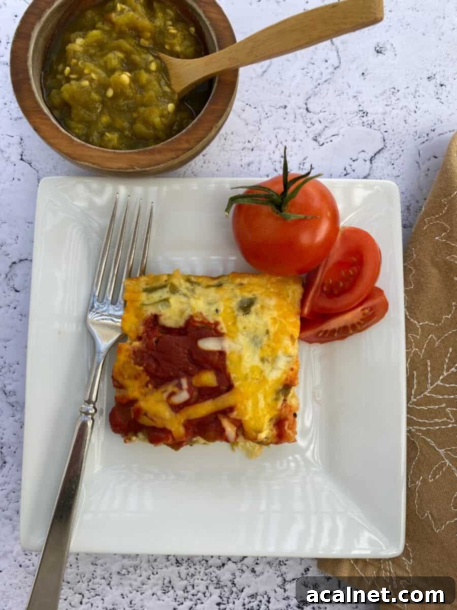 Fiesta Green Chile Egg Casserole 8 A plate with a serving of chili relleno casserole, fresh tomatoes, and a fork. A bowl of salsa and a napkin are on the side.
