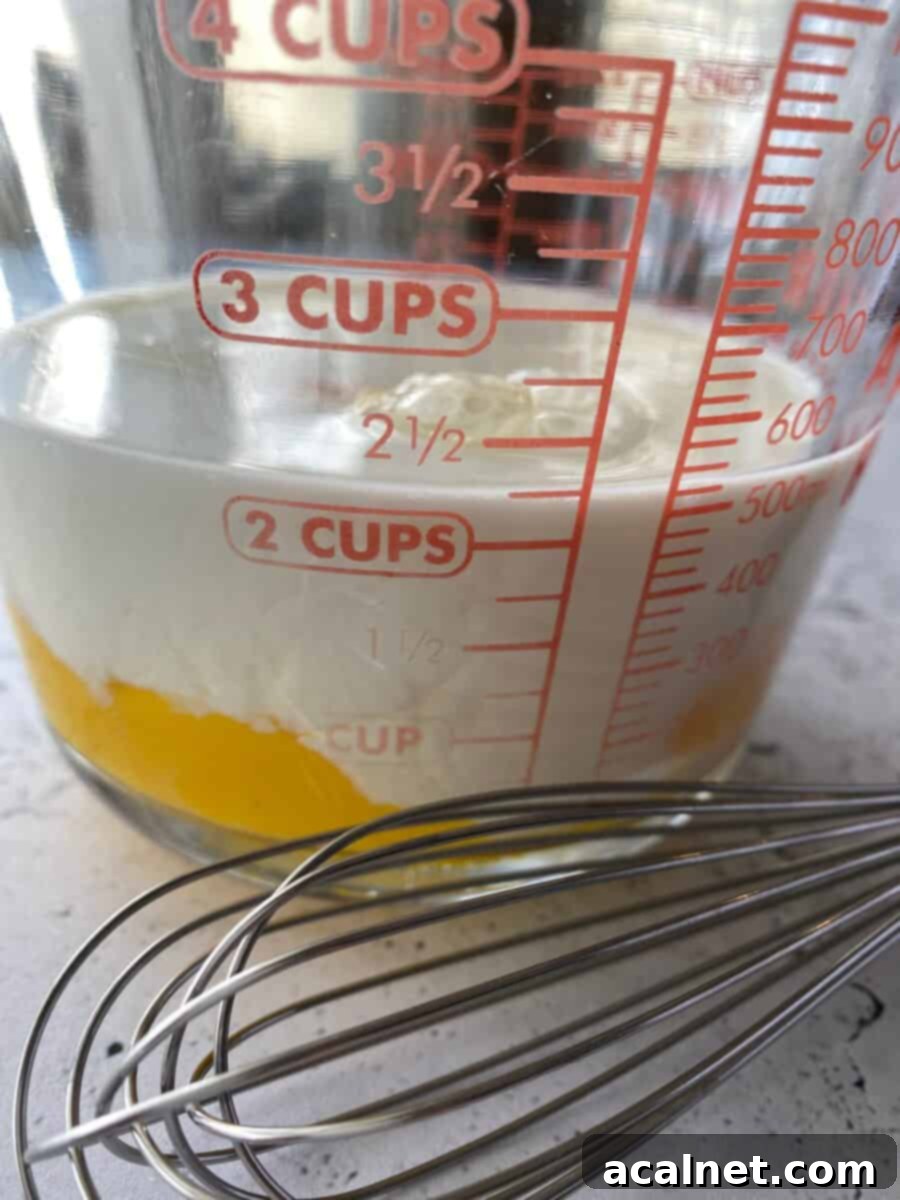 Milk and eggs in a measuring cup with a whisk on the side.