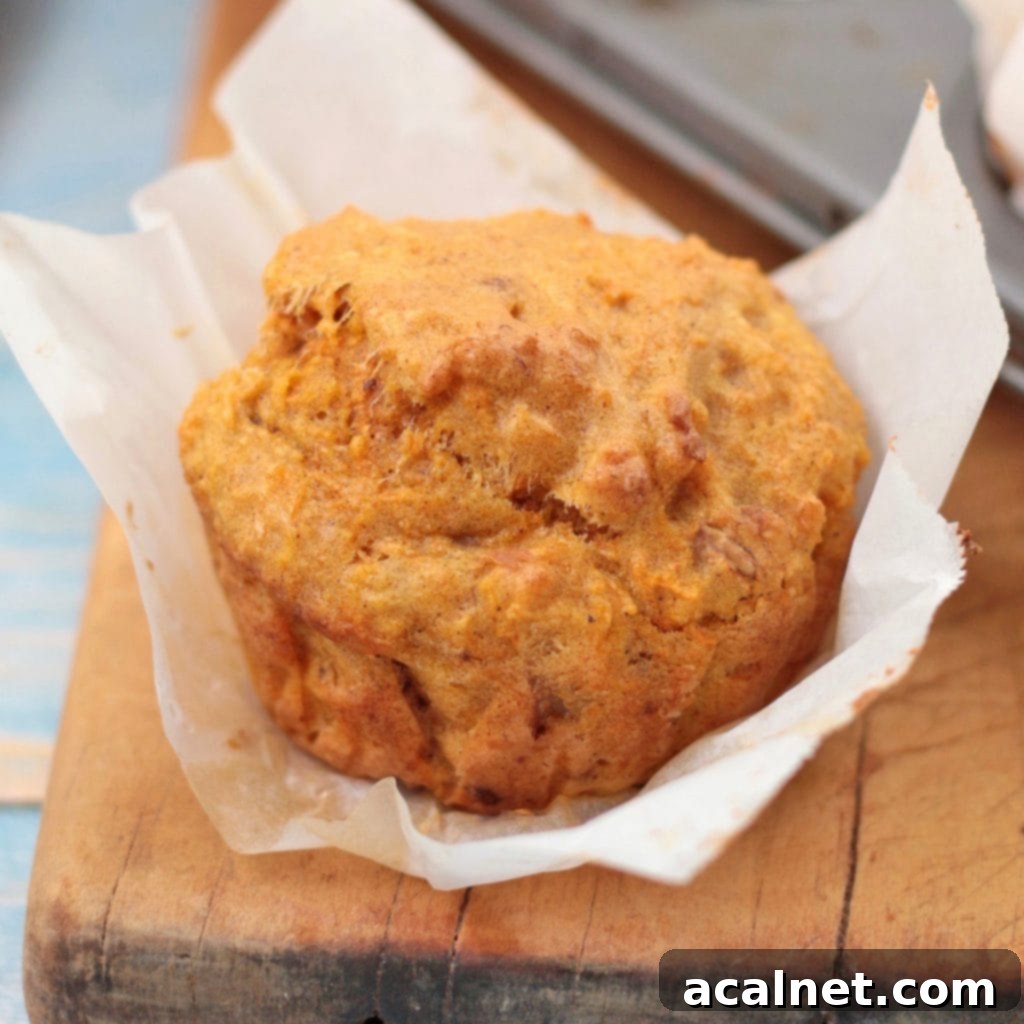 A freshly baked vegan carrot muffin, unwrapped and resting on a rustic wooden board, ready to be enjoyed. Highlighted are its moist texture and the subtle speckles of carrot and spice.
