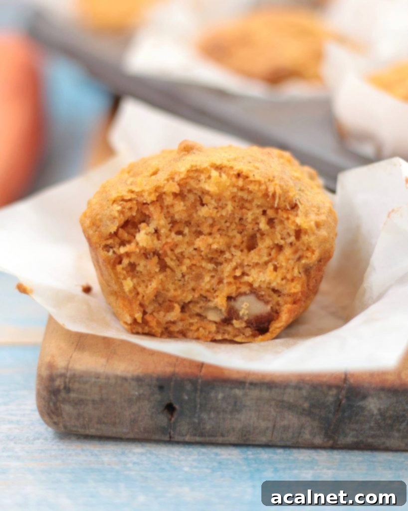 A perfectly baked vegan carrot muffin cut in half, revealing its moist, tender crumb and speckles of grated carrots and apples. The soft, fluffy texture is inviting.
