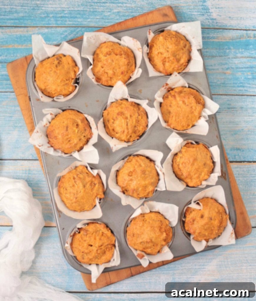 Freshly baked vegan carrot muffins cooling in a muffin pan, viewed from above. Their golden tops indicate they are perfectly cooked and ready to be enjoyed.