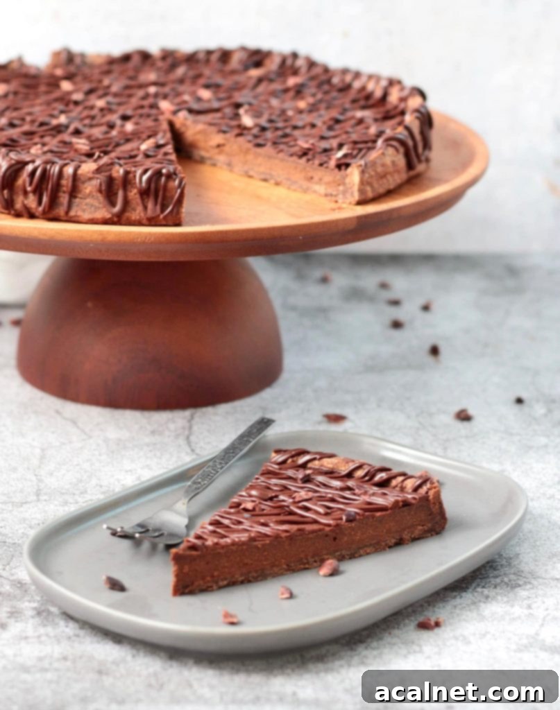 Decadent French Chocolate Tart 5 One slice of the tart on a grey plate with the rest of the tart over a cake stand in the background