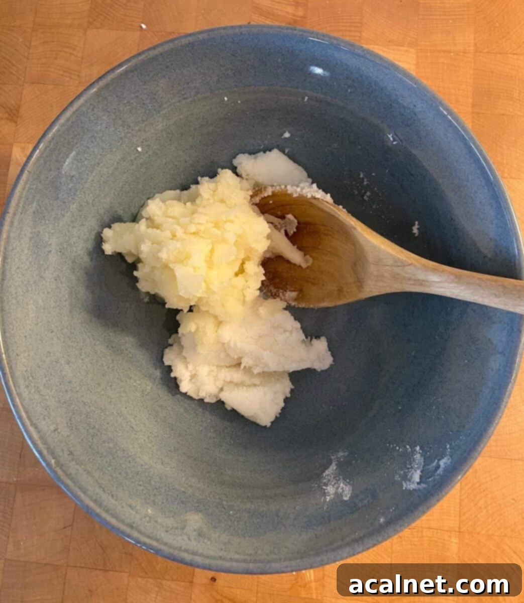 A bowl containing smooth mashed potatoes, shortening, and sugar, ready to be mixed with a wooden spoon.