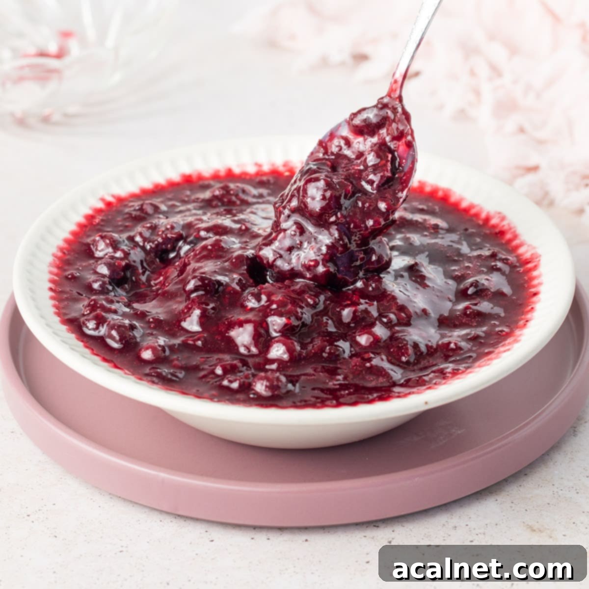 White bowl filled with berry compote on top of a pink plate.