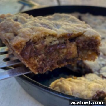 A chocolate chip bar cookie on a spatula, lifted out of a cast iron skillet, set on an outdoor table.