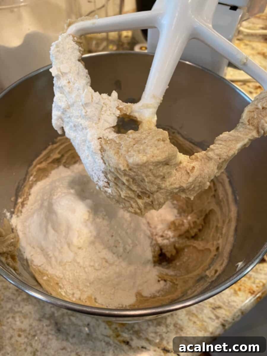 Dry ingredients are mixed with wet ingredients in a stand mixer bowl, with the mixing paddle poised above the dough for chocolate chip bars.