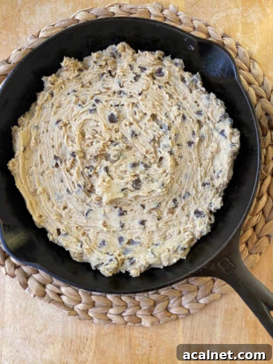 Unbaked chocolate chip bar cookie dough is spread evenly in a cast iron skillet, ready for baking.