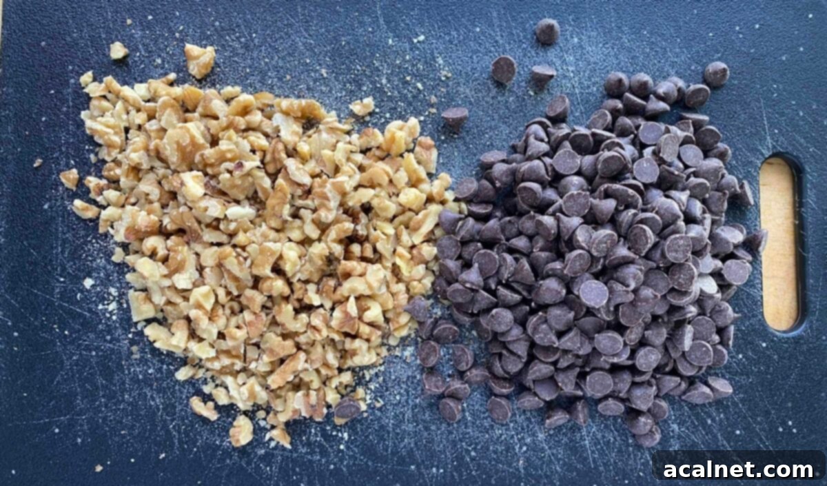 A generous scattering of chopped walnuts and semi-sweet chocolate chips on a cutting board, ready to be incorporated into the cookie dough.