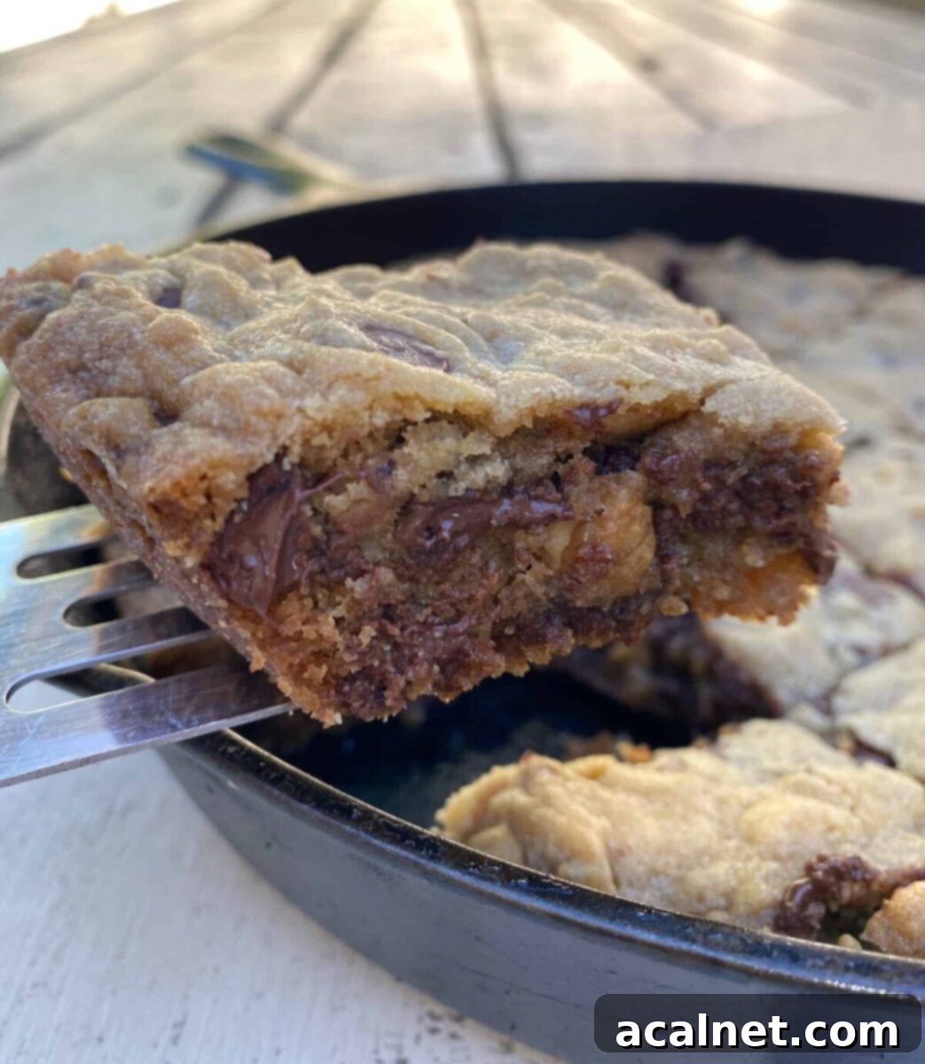 A perfectly baked chocolate chip bar cookie, lifted on a spatula from a cast iron skillet, showcasing its rich texture and melty chocolate.