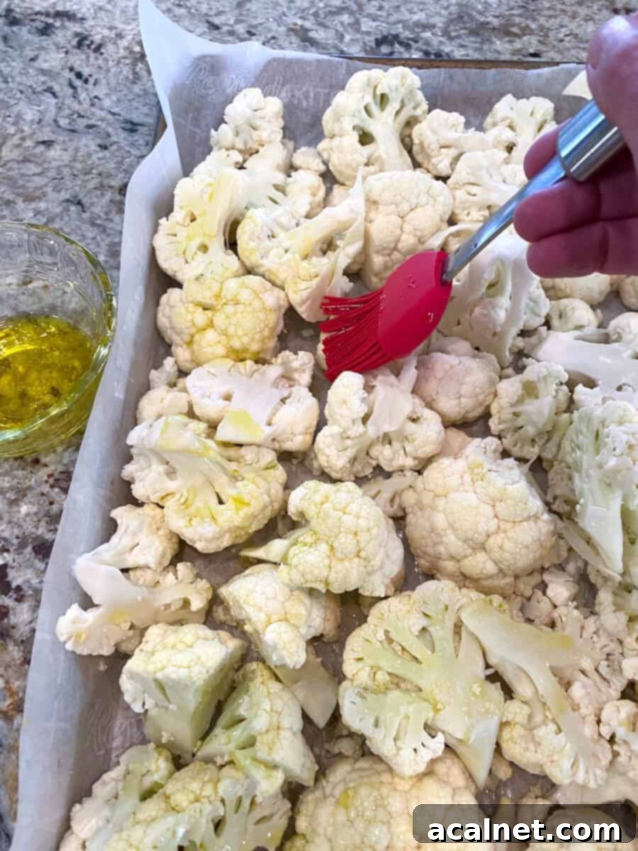 Everything-Spiced Cauliflower Hummus 5 Raw cauliflower pieces on a baking pan being brushed with olive oil for even coating.