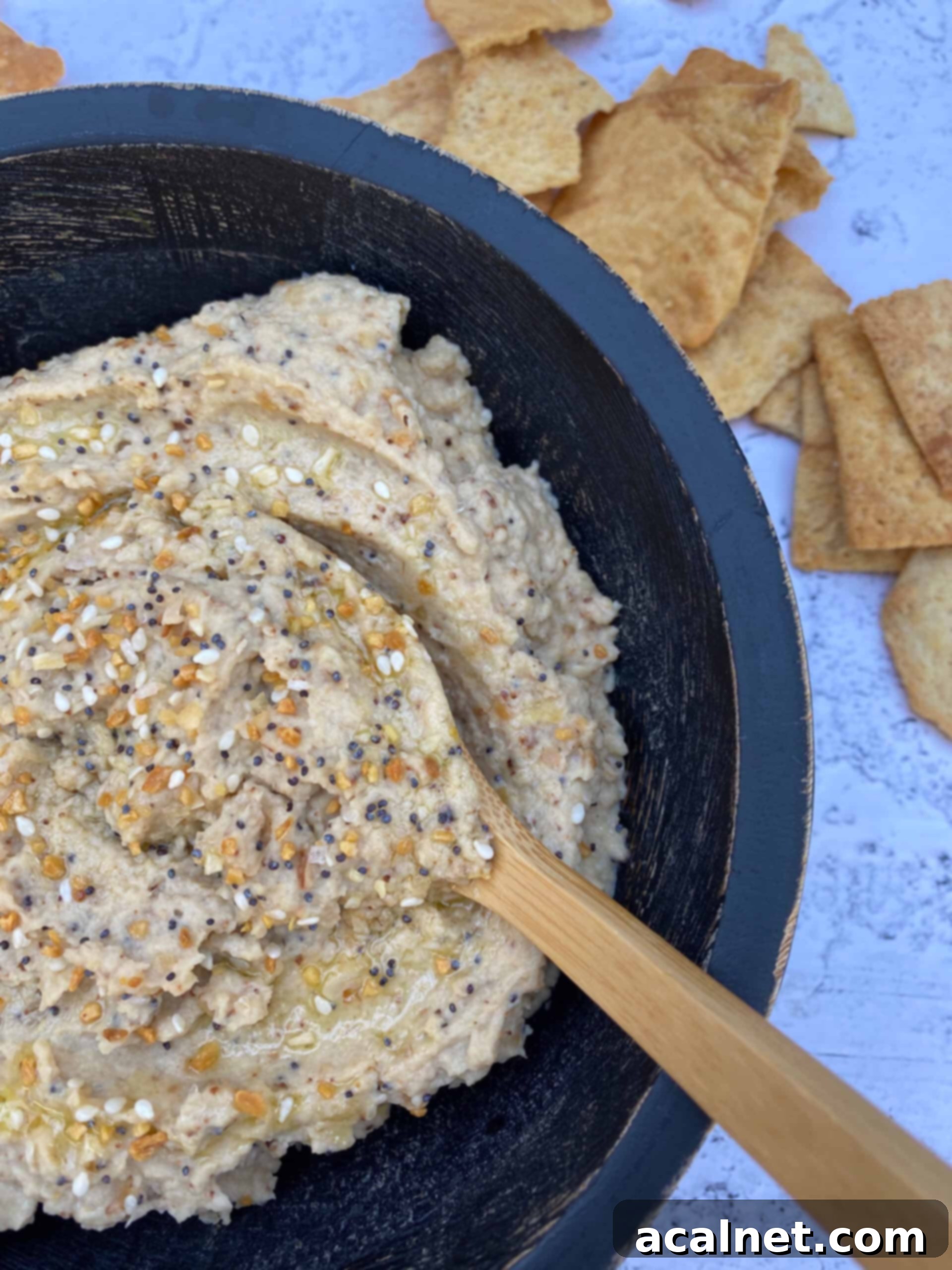 Everything-Spiced Cauliflower Hummus 7 Hummus in a bowl with a small wooden spoon and pita chips on the side, ready for serving.
