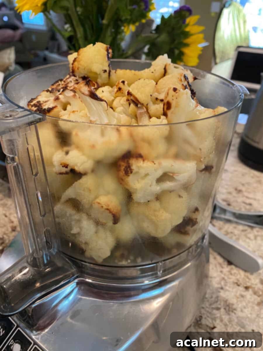 Everything-Spiced Cauliflower Hummus 8 Cauliflower Hummus ingredients, including roasted cauliflower, garlic, and tahini, ready in the bowl of a food processor before blending.