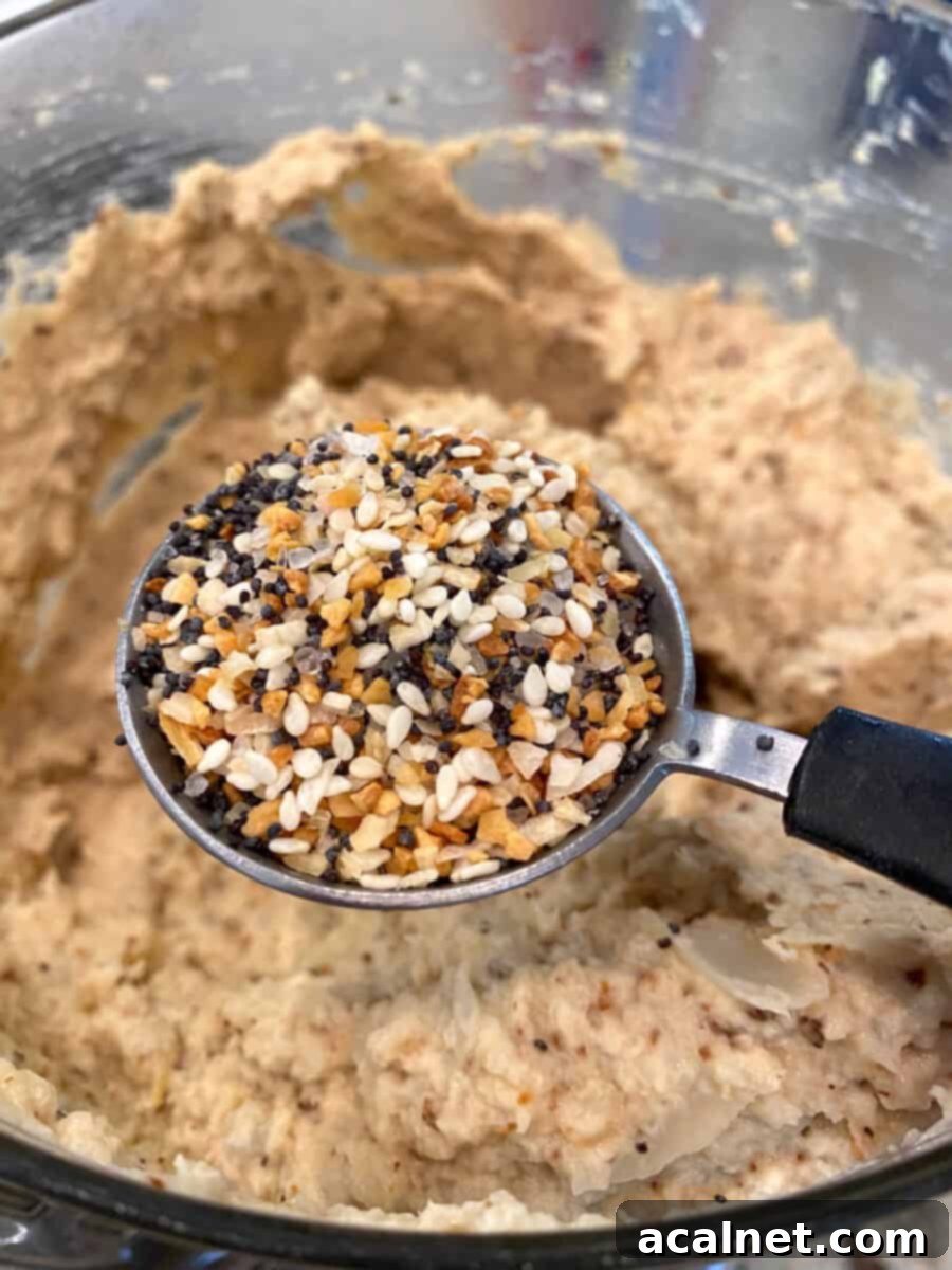 Everything-Spiced Cauliflower Hummus 9 A tablespoon of Everything Bagel seasoning held over freshly blended cauliflower hummus, ready to be added.