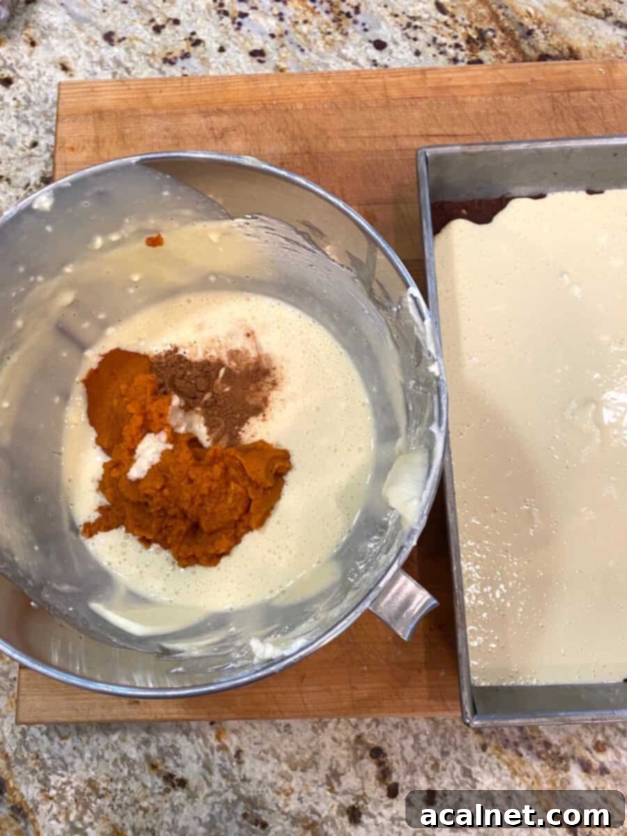 Spiced Pumpkin Swirl Cheesecake Bars 7 A mixing bowl with pumpkin puree and spices sits beside a baking pan containing the plain cream cheese batter, ready for the marbling process.