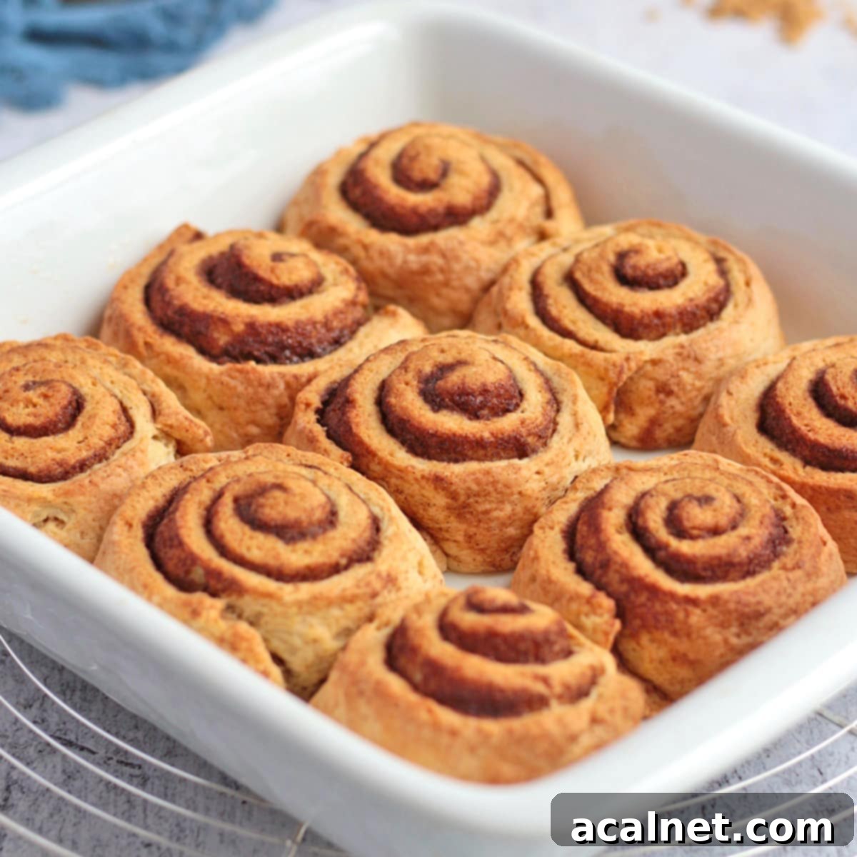Nine warm, golden brown no-yeast cinnamon rolls with a generous drizzle of white icing, baked in a white ceramic baking dish, ready to be enjoyed.