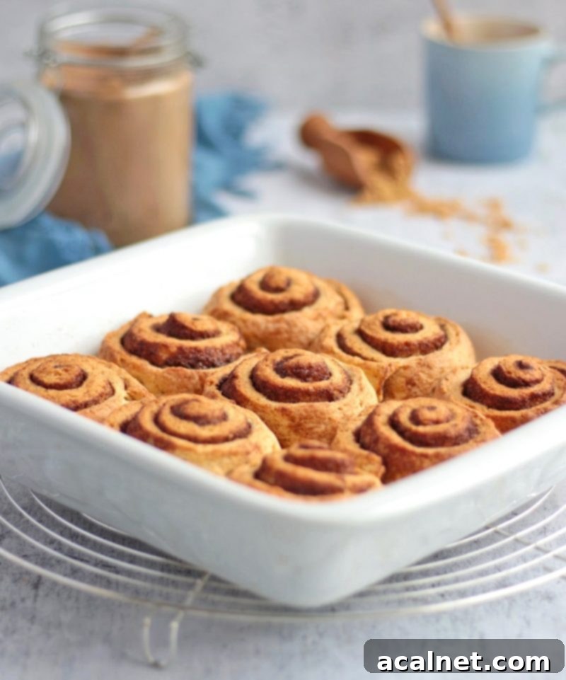 Freshly baked no-yeast cinnamon rolls, golden and puffed, cooling in a white ceramic dish on a round metal rack, ready for icing.