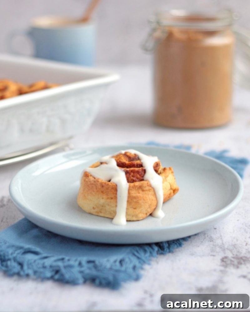 A single no-yeast cinnamon roll on a blue plate, beautifully drizzled with white Greek yogurt icing, with a fork poised to take a bite.