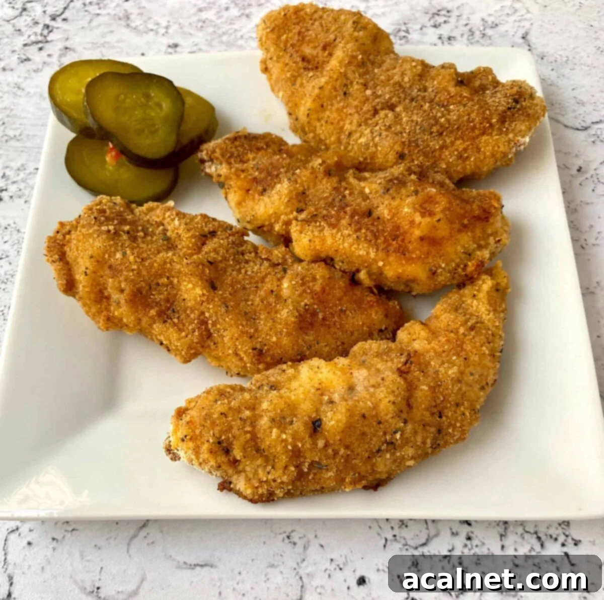 Golden Buttermilk Chicken Tenders 2 Chicken strips on a serving plate with pickles on the side