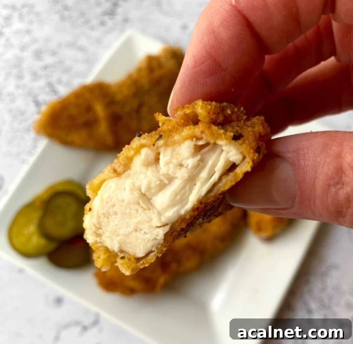 Golden Buttermilk Chicken Tenders 12 A chicken strip with a bite taken out of it, being held in a hand