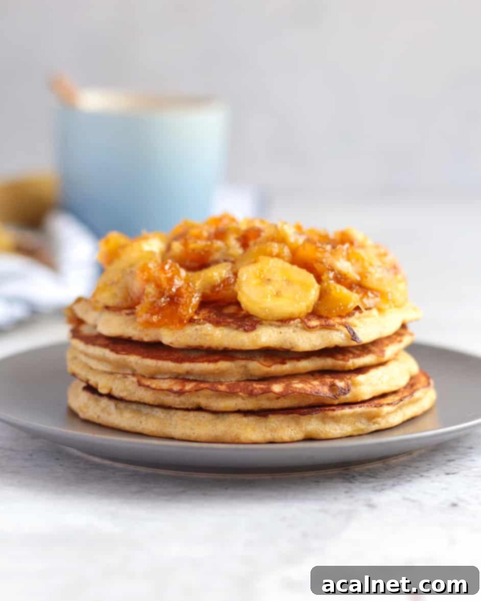 Stack of pancake topped with banana topping on a grey plate behind a white background.