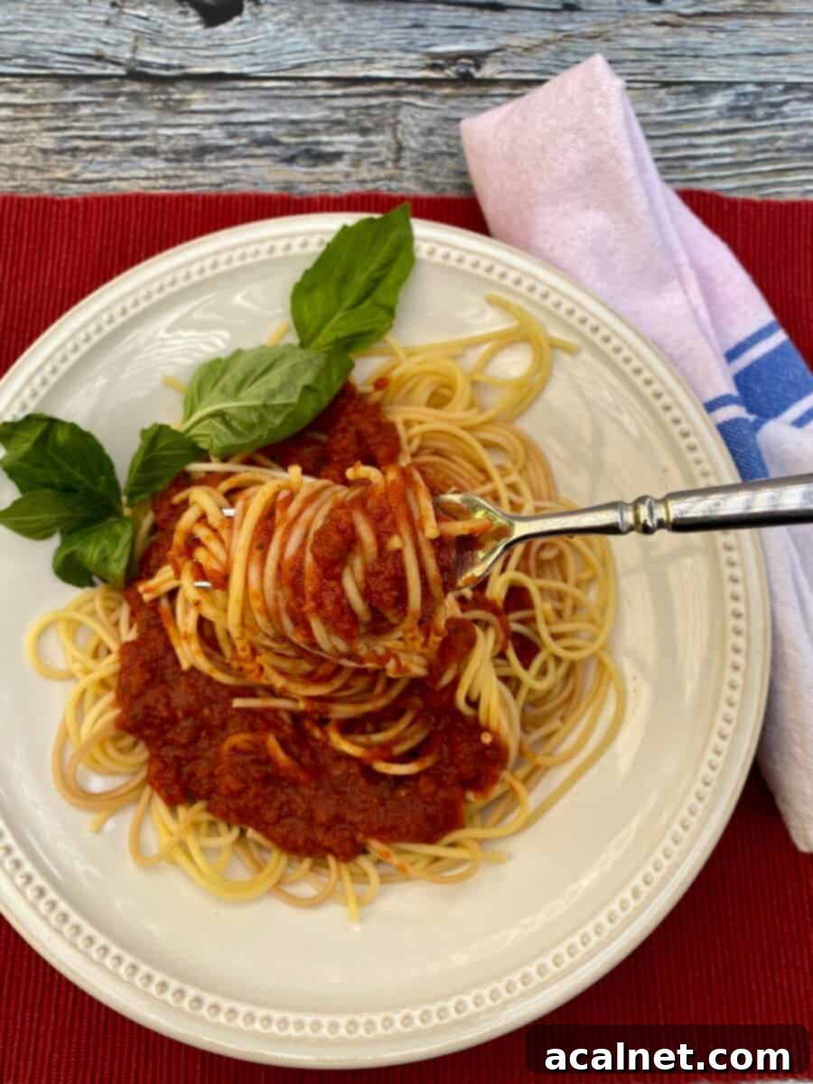 Spaghetti sauce and pasta noodles on a plate with a fork, basil on the edge and a napkin