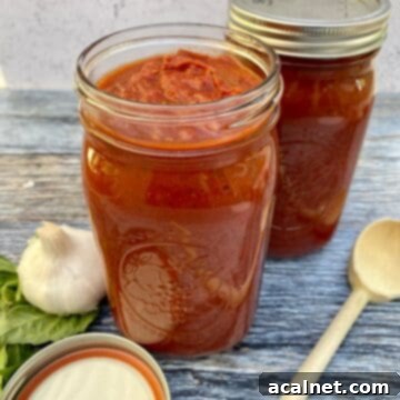 Sunday gravy in jars with a lid and a wooden spoon on the side next to a bulb of garlic and fresh basil
