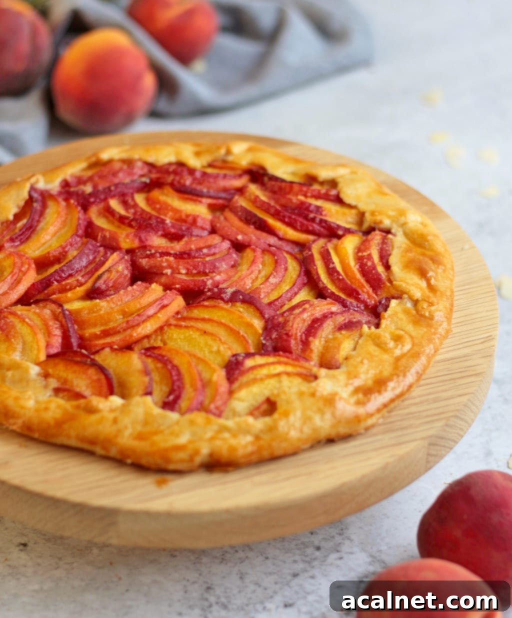 Side view of the Almond Peach Galette on a wooden cake stand, highlighting the folded crust and baked peach slices.