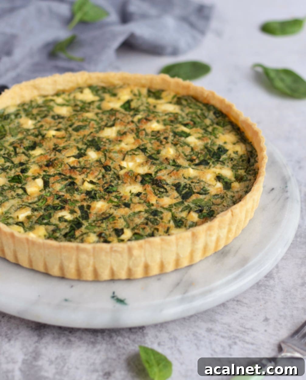 A beautifully baked Spinach and Feta Quiche, viewed from the side to show its golden crust and creamy filling.