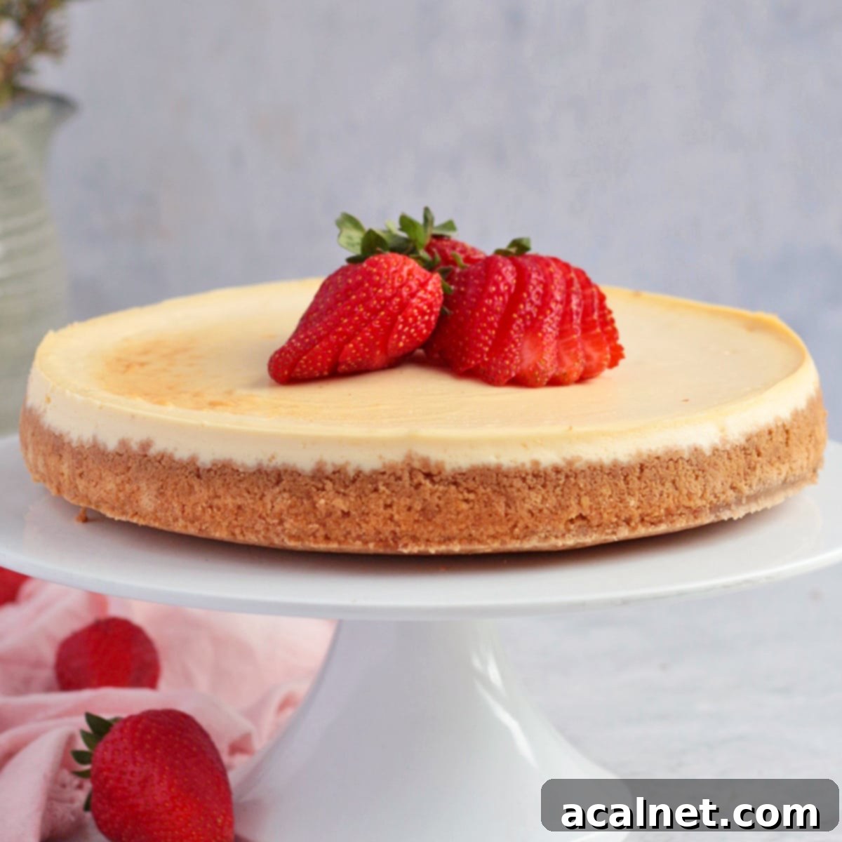Cheesecake on a white cake stand topped with strawberries