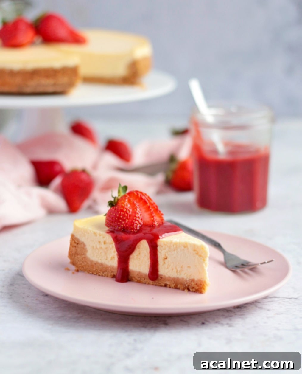 One slice of ricotta cheesecake with strawberry sauce and cheesecake on a cake stand in the background