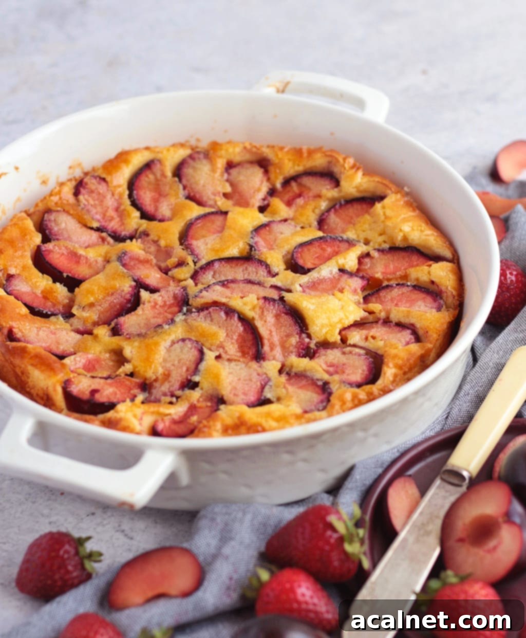 Simple Plum Clafoutis 3 Side view of the baked plum clafoutis in a white ceramic dish, showing its rich custard texture and visible plums.