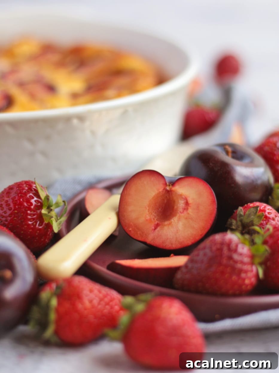 Simple Plum Clafoutis 4 Photo of a plum sliced in half, surrounded by fresh strawberries and whole plums, highlighting the fresh fruit.