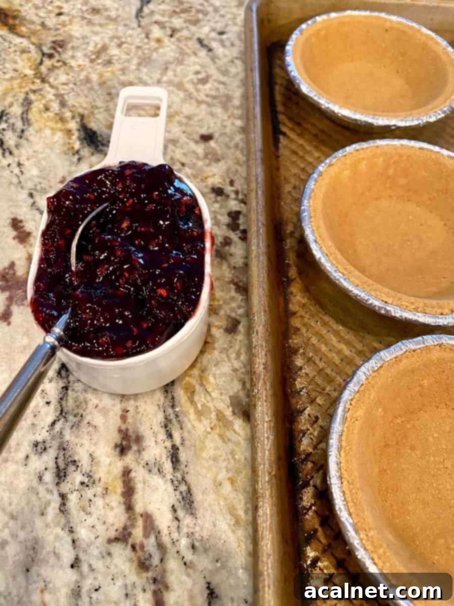 A half cup of jam next to a baking sheet filled with mini pie crusts