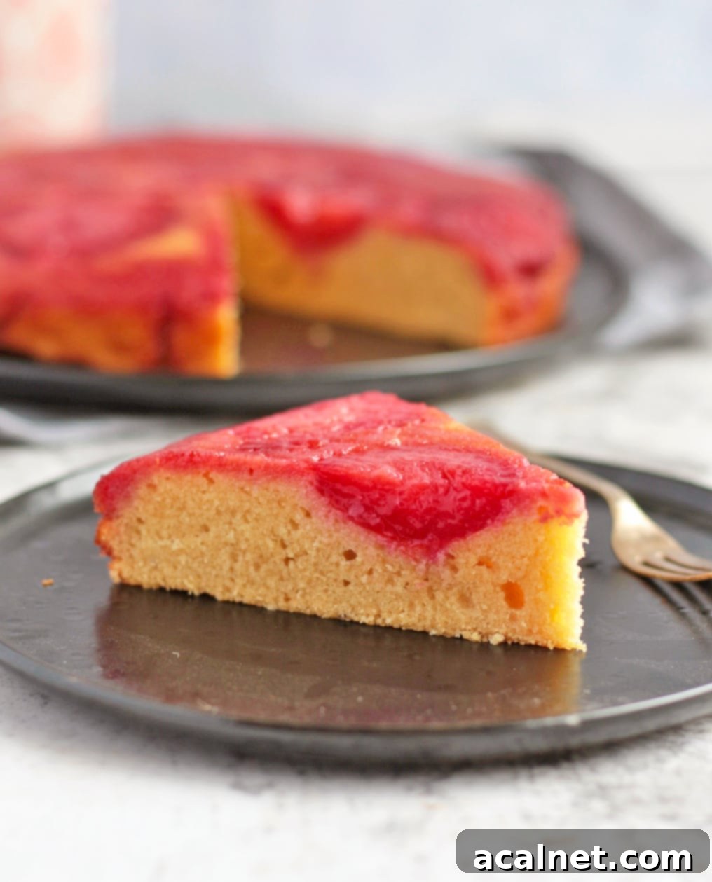 A perfectly baked slice of Plum Upside Down Cake on a black plate.