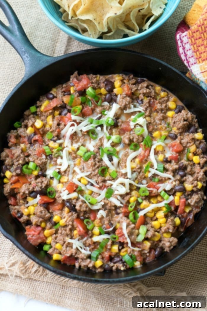 Taco Dip with Ground Beef in a skillet, topped with cheese, olives, and tomatoes.