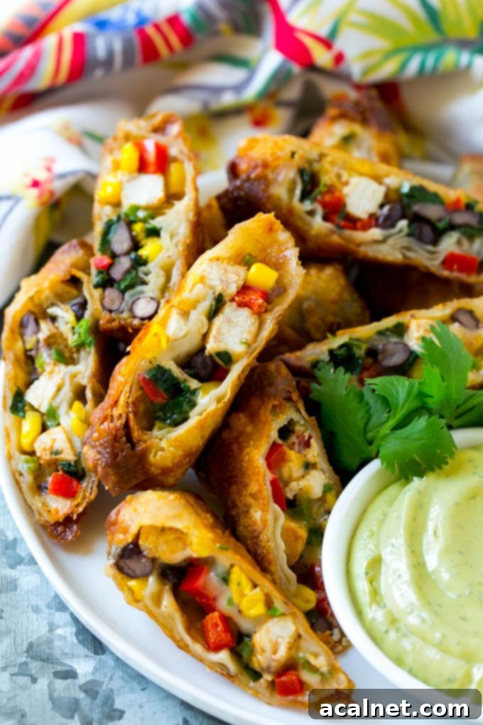 Southwestern Egg Rolls cut in half, revealing a colorful filling, served with a dipping sauce.