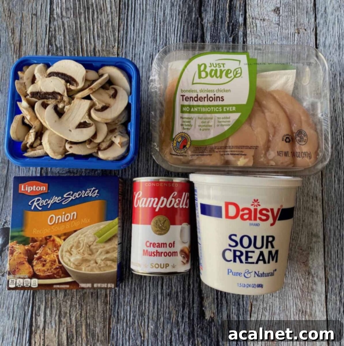 Creamy Chicken and Mushroom Stroganoff 3 Raw chicken stroganoff ingredients including chicken tenders, mushrooms, sour cream, and soup mix on wooden planks.