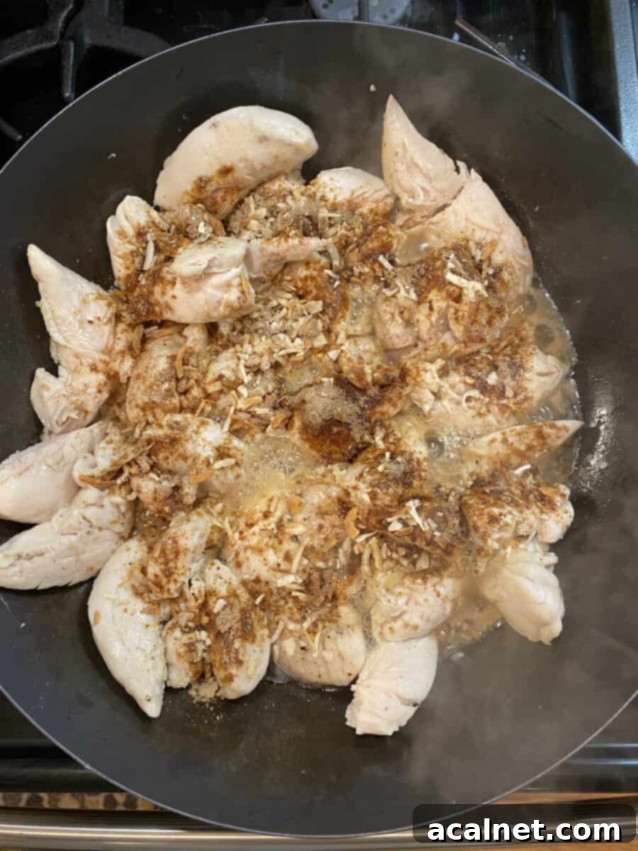 Creamy Chicken and Mushroom Stroganoff 4 Onion soup mix being sprinkled on partially cooked chicken in a large skillet with a wooden spoon.