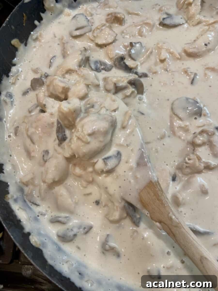 Creamy Chicken and Mushroom Stroganoff 8 Stroganoff cooking in a skillet on the stove with a wooden spoon stirring the contents, showcasing the creamy texture.