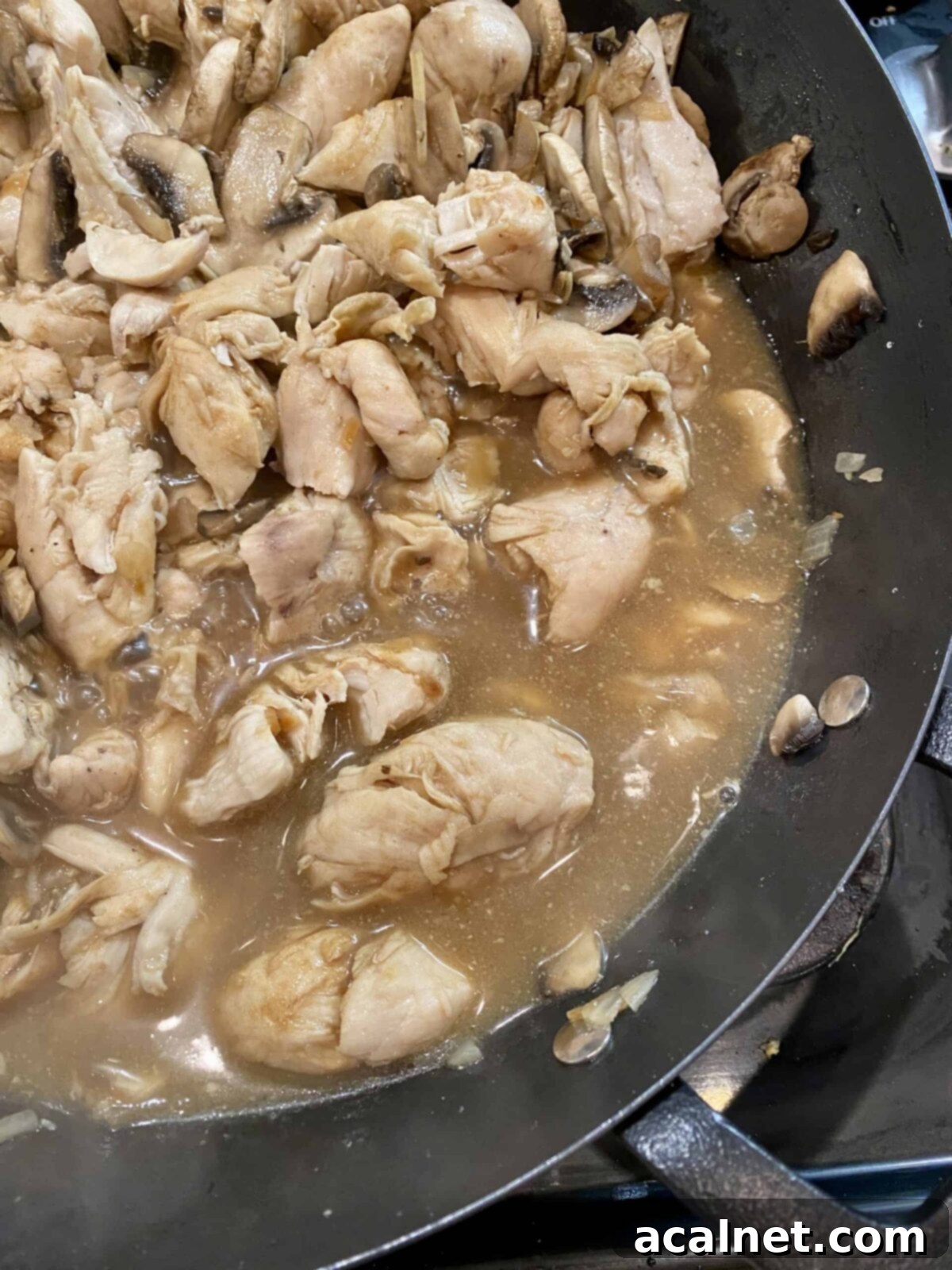 Creamy Chicken and Mushroom Stroganoff 9 Simmering sauce with chicken in a skillet on the stove, showing a rich, brown color.
