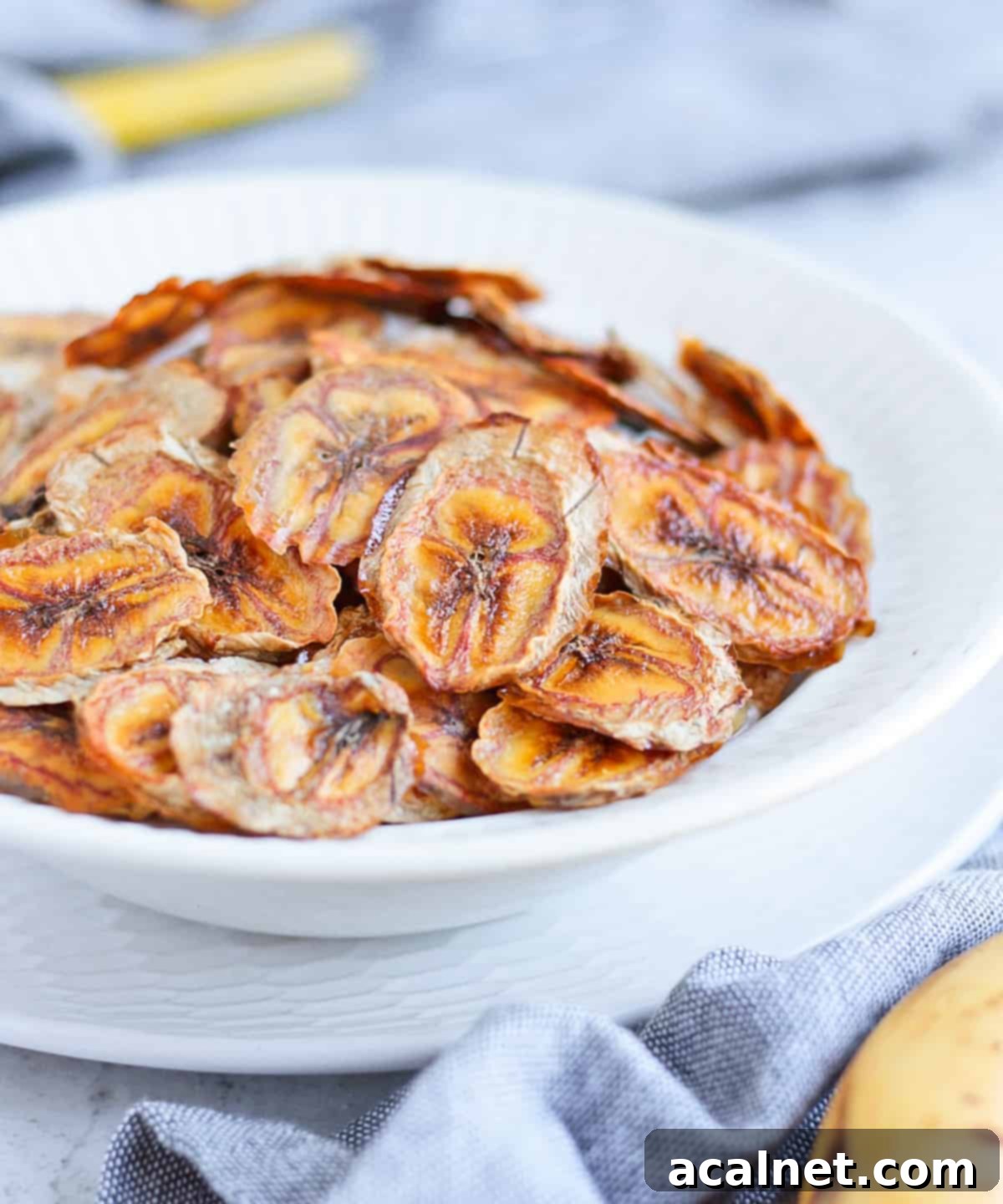 Crispy Oven-Baked Banana Chips 5 Close-up of healthy homemade banana chips in a white bowl, showing their crispy texture.