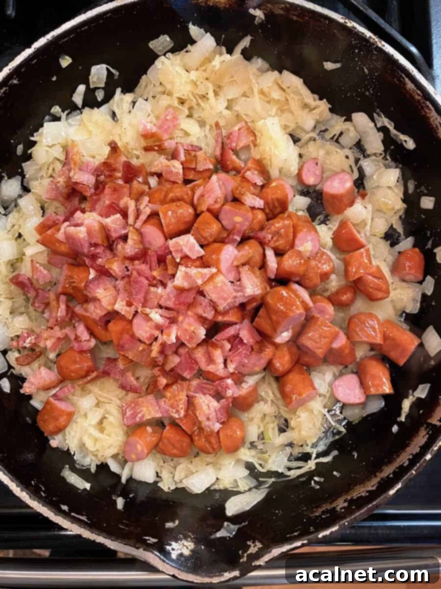Onions, sauerkraut, and little smokies, topped with diced bacon, combining flavors in a cast iron skillet.