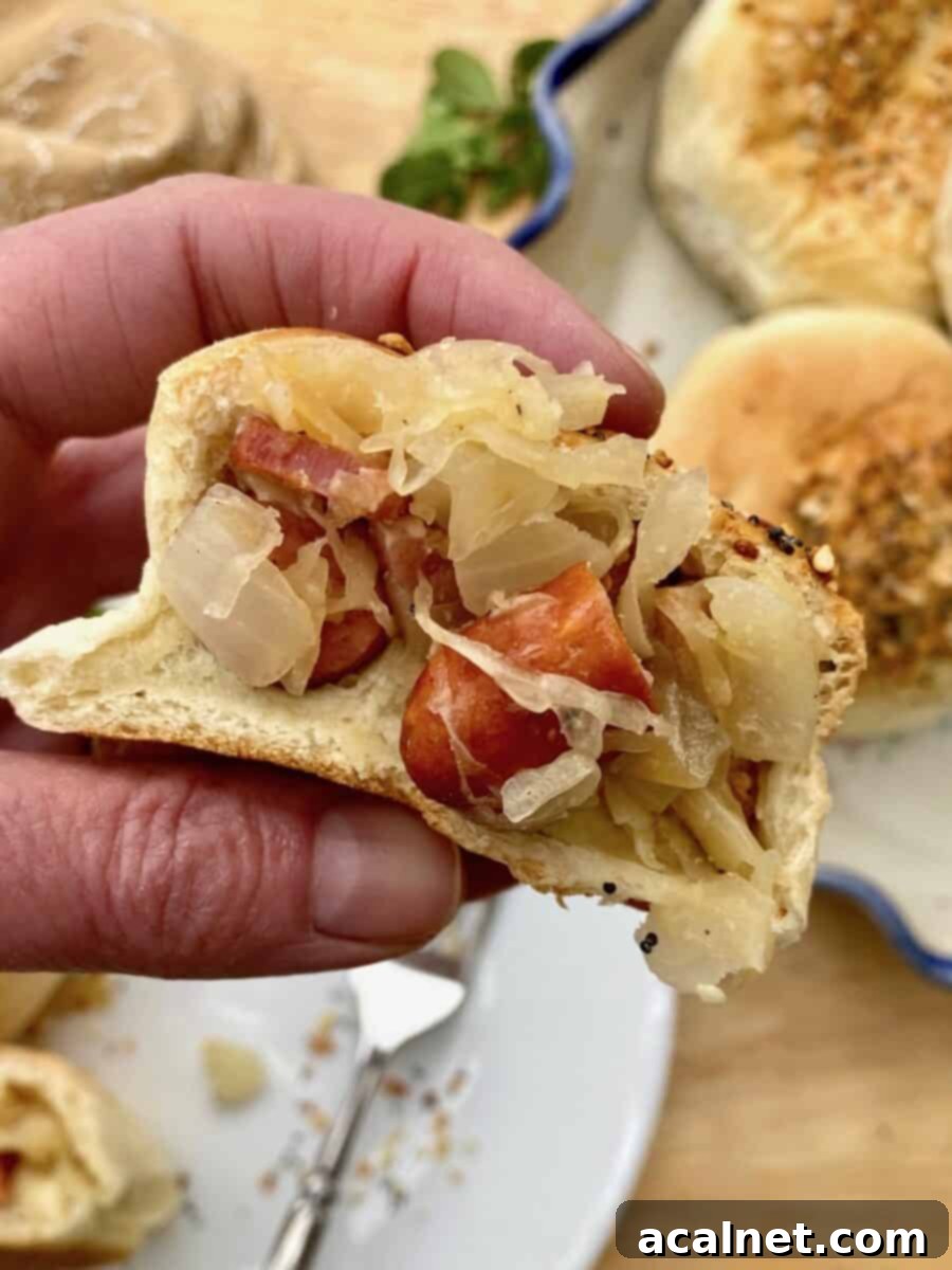 A Grown-Up Pig in a Blanket, cut in half and held in a hand, ready to be enjoyed.