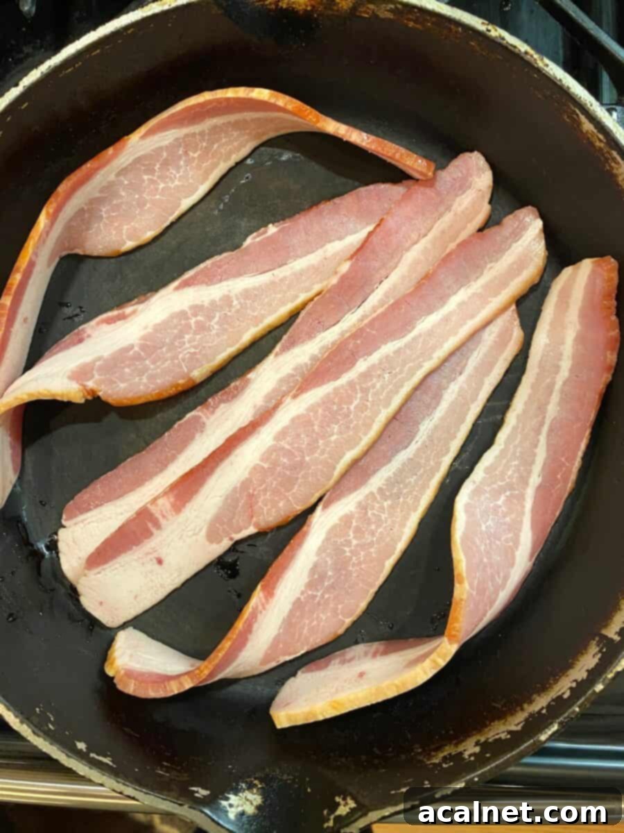 Six slices of bacon sizzling in a cast iron skillet, cooking to a perfect crisp.