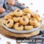 Sadece 3 Malzemeyle Pratik Glutensiz Sütsüz Badem Kurabiyesi 8 Stack of almond cookies on a white plate over a wooden board.