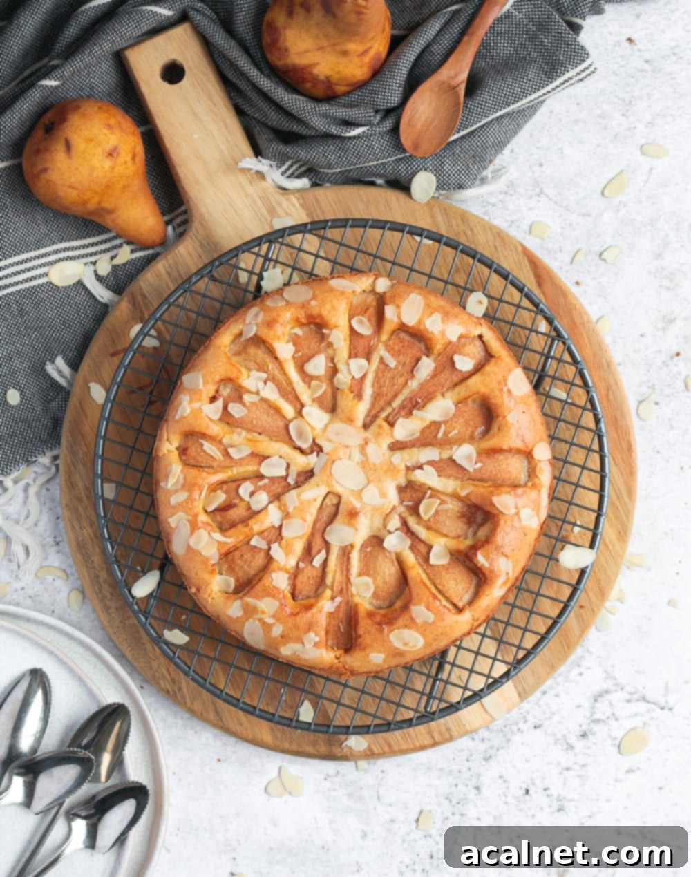 A flatlay shot of the golden-brown Flourless Pear Almond Cake on a rustic wooden board, showing its beautiful top with pear slices and flaked almonds.